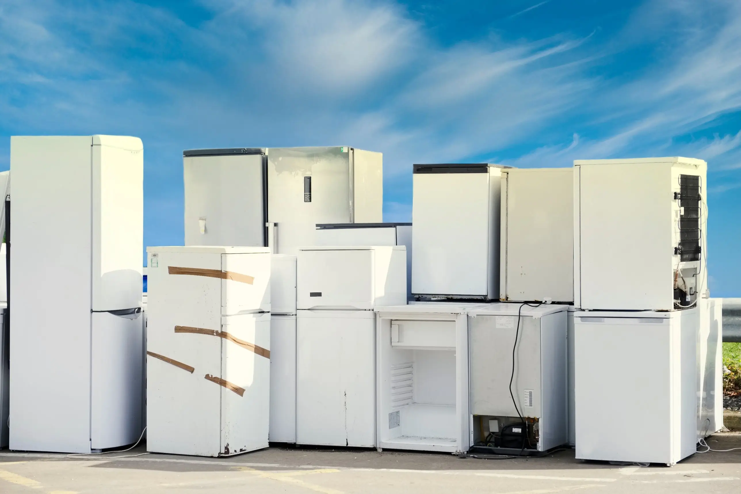 Old white refrigerators and freezers standing in a row outdoors on a sunny day