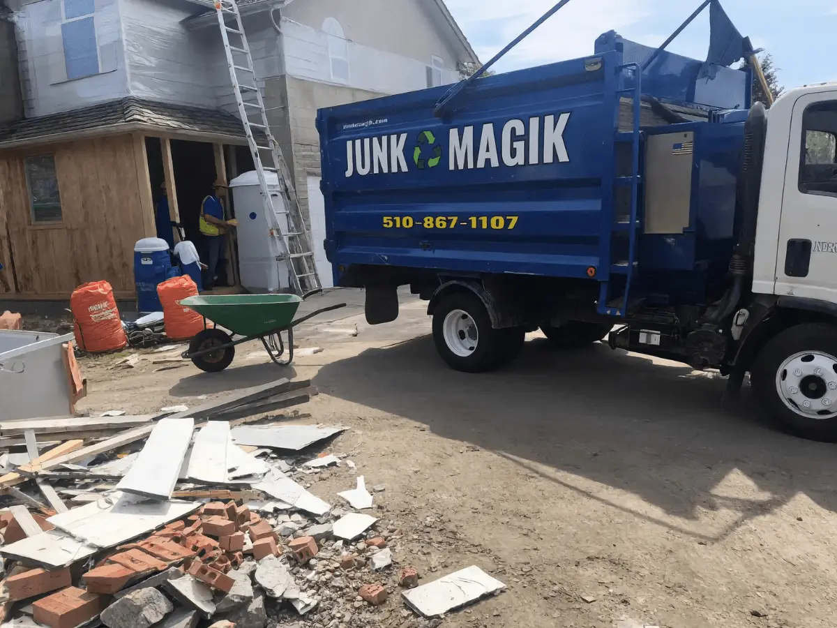 A kitchen mid-demolition with a pile of torn-out drywall on the floor, stripped wall studs, a stepladder, debris buckets and a shop vacuum